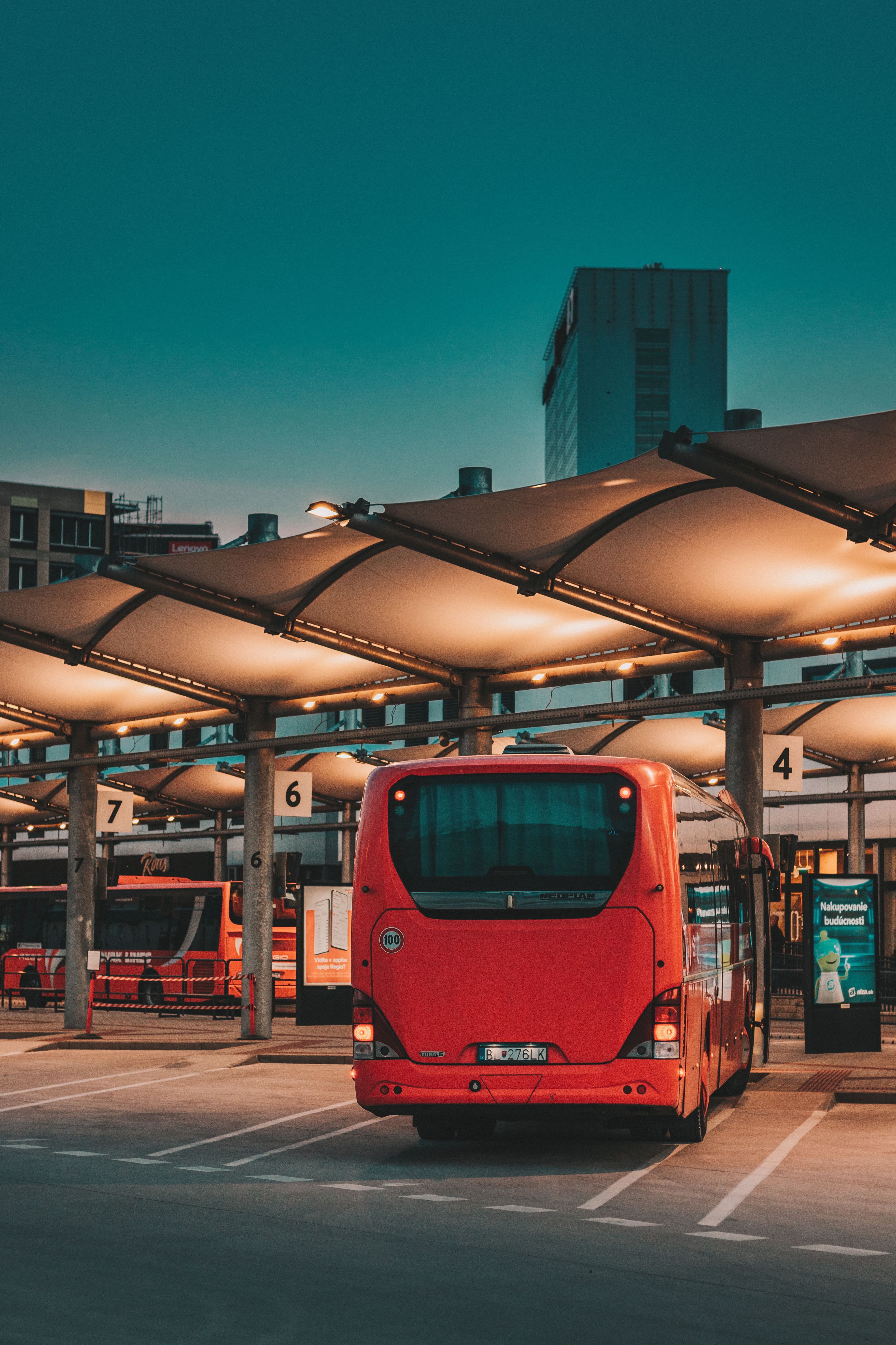 Um ônibus vermelho vibrante estacionado em uma estação de ônibus da cidade durante a noite, sob toldos iluminados.