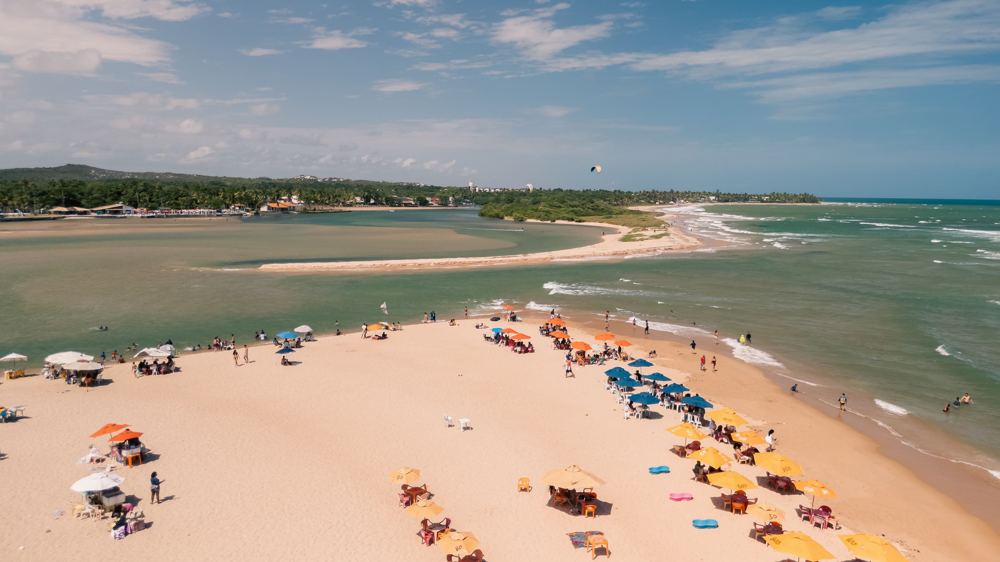 Vista aérea da vibrante praia de Lauro de Freitas, Bahia, com guarda-sóis coloridos e banhistas.