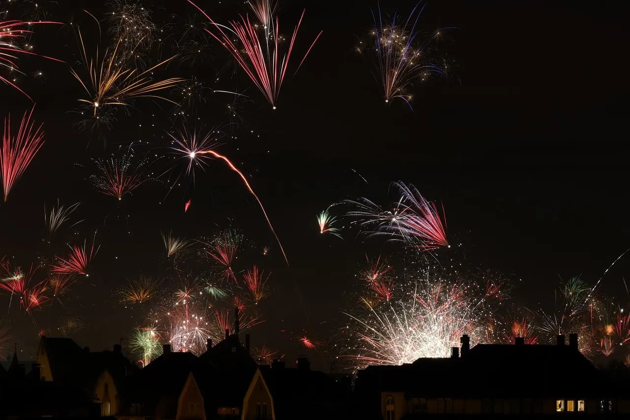 Fogos de artifício coloridos explodindo no céu noturno sobre telhados de casas