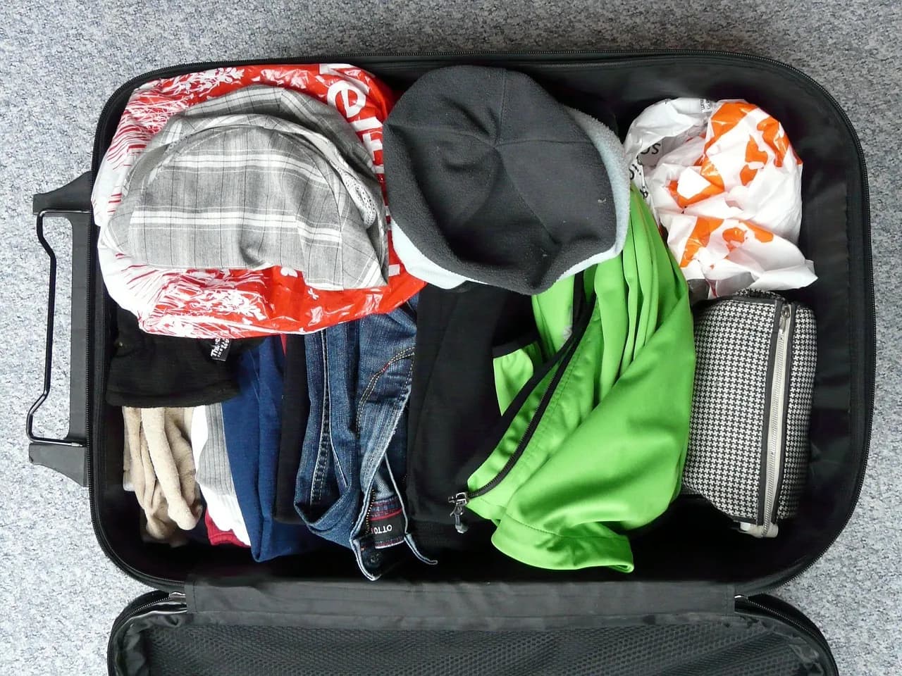 Mala de viagem preta aberta, cheia de roupas e uma necessaire, vista de cima