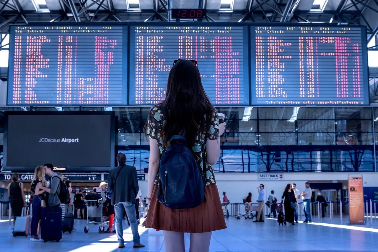 Mulher de costas observa um grande painel eletrônico com informações de voos em aeroporto