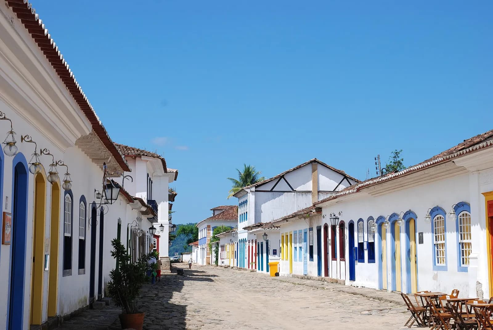 Rua de paralelepípedos vazia no centro histórico de Paraty, com casas coloniais brancas e coloridas sob céu azul